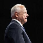 Elderly man in suit speaking on stage