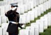 A soldier in uniform saluting in a military cemetery with white gravestones in the background