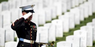 A soldier in uniform saluting in a military cemetery with white gravestones in the background
