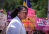 A woman speaking at a protest with signs advocating for abortion rights in the background