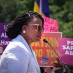 A woman speaking at a protest with signs advocating for abortion rights in the background