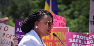 A woman speaking at a protest with signs advocating for abortion rights in the background