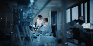 Two scientists working in a laboratory with a microscope and computer screens