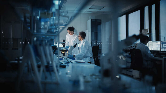 Two scientists working in a laboratory with a microscope and computer screens