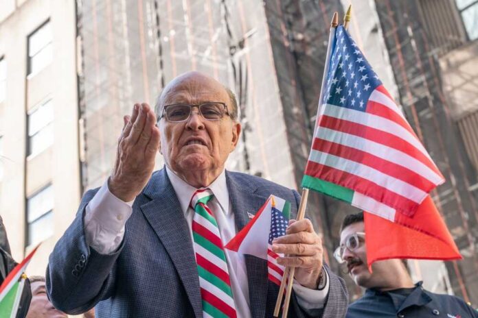 A man passionately speaking at a rally while holding American flags