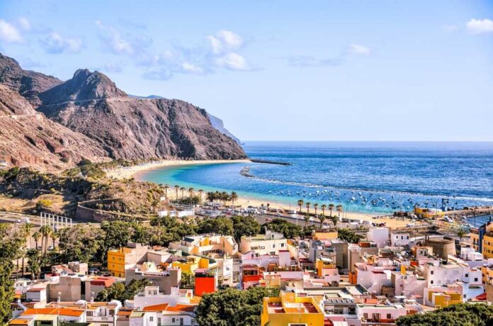 Scenic view of a beach with mountains and colorful buildings in the foreground