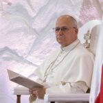 Pope seated in a ceremonial chair with flags in the background