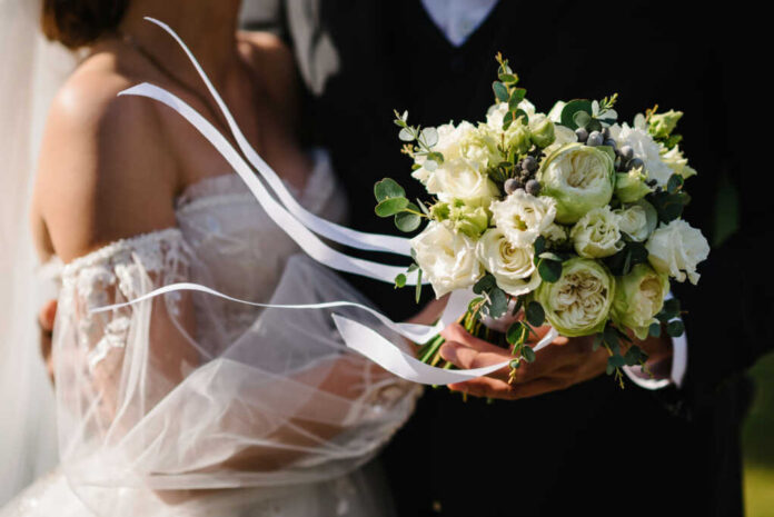 Bride holding white flower bouquet with ribbons