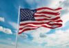 Homeowners Fight HOA Over Patriotic Displays American flag waving on a flagpole against a blue sky with clouds