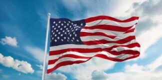 American flag waving on a flagpole against a blue sky with clouds