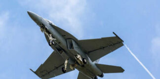 Military jet flying with vapor trails visible