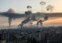 Gaza Waterfront Hit—Facts Still Missing City skyline with rising smoke and birds in sky.