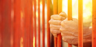 Hands gripping orange prison bars with sunlight in the background