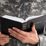 Woke Purge Or Cleanup? Pentagon Slashes Faiths Person in uniform holding an open Bible