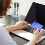 Paycheck ‘Victory’ Hides A Painful Bill Person holding a credit card while using a laptop