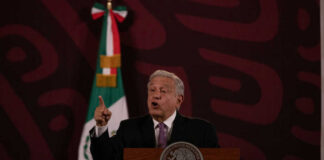 Man speaking at podium with Mexican flag behind him