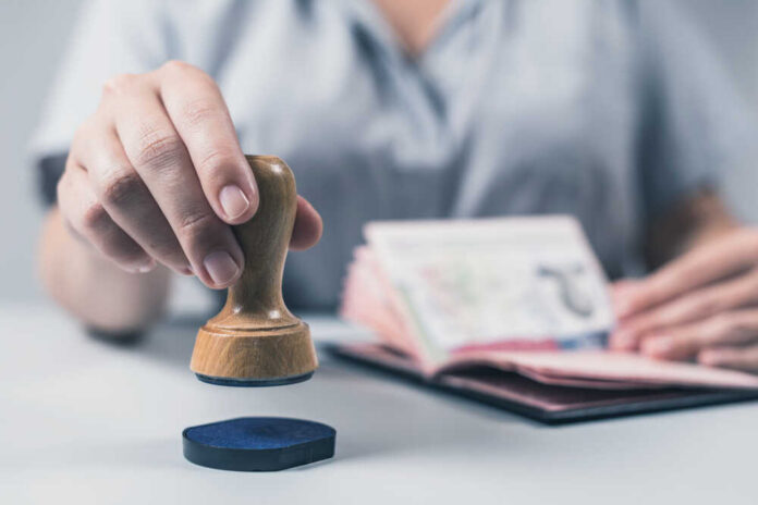 Immigration,And,Passport,Control,At,The,Airport.,Woman,Border,Control A hand holding a wooden stamp above a passport on a table