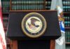 A Sealed Filing Took An Unusual Detour Podium with the Department of Justice seal and American flag in the background
