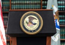 A Sealed Filing Took An Unusual Detour Podium with the Department of Justice seal and American flag in the background