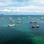 Hormuz Tensions Put Energy Markets On Edge Aerial view of numerous cargo ships anchored in a blue ocean