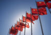 Beijing Tightens Grip On Global Capital Multiple Chinese flags waving against a clear blue sky