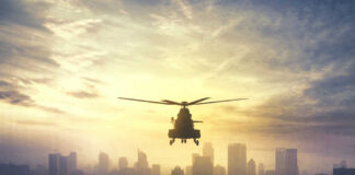 Silhouette of a helicopter flying over a city skyline at sunset