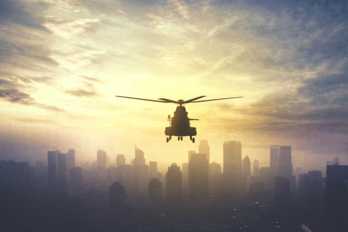 Silhouette,Of,Military,Helicopter,Hovering,Over,Downtown,,Shot,At,Sunset Silhouette of a helicopter flying over a city skyline at sunset