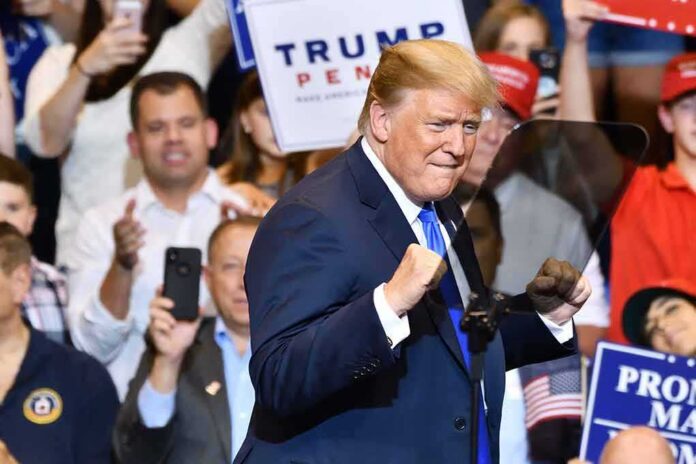man in suit raising fists at a rally podium