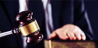 Judge's gavel striking block with hand on book in background
