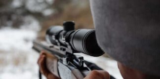 person aiming a rifle with a scope outdoors