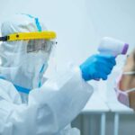 Pandemic Flashback: Cuomo’s Words Haunt Back Healthcare worker in PPE checks patient temperature with infrared thermometer