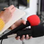 Musk’s Midterm Money Machine Is Now Moving Journalist holding two microphones while writing in a notebook