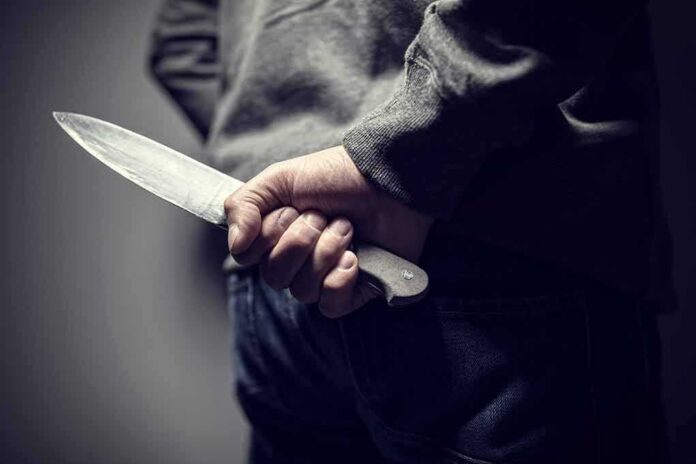 shutterstock_1109521271 person holding a large knife behind their back