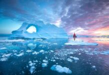 Greenland Control Deal Ignites Questions Iceberg with arch and red-sailed boat at colorful sunset