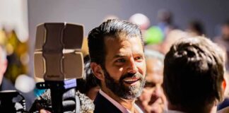 man with beard in suit speaking to people at crowded event