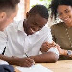 Smiling man signs a document with supportive couple beside him