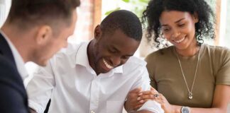 Smiling man signs a document with supportive couple beside him
