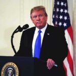 Trump Corrals Musk, Zuck – What Did They Sign? man at podium with microphone and US flag