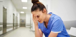 Nurse in blue scrubs sitting with head in hand