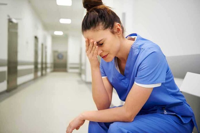Nurse in blue scrubs sitting with head in hand