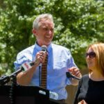 Robert F. Kennedy Jr. speaking at an outdoor podium with a woman beside him