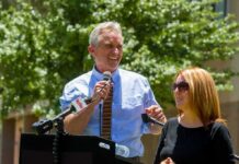 Robert F. Kennedy Jr. speaking at an outdoor podium with a woman beside him