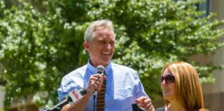 Robert F. Kennedy Jr. speaking at an outdoor podium with a woman beside him