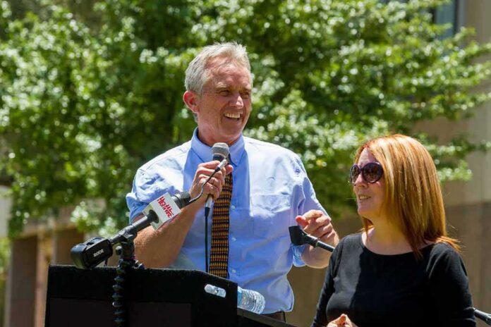 Robert F. Kennedy Jr. speaking at an outdoor podium with a woman beside him