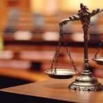 Immunity Shattered: Trial Greenlit for Brawl bronze balance scales on a courtroom desk