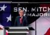 McConnell Rolls In – And The Vote Flips? Man in suit speaking at a podium on a stage
