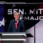 McConnell Rolls In – And The Vote Flips? Man in suit speaking at a podium on a stage