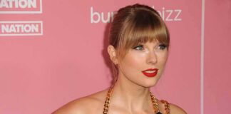 Taylor Swift on a pink carpet in a black dress with gold chain straps