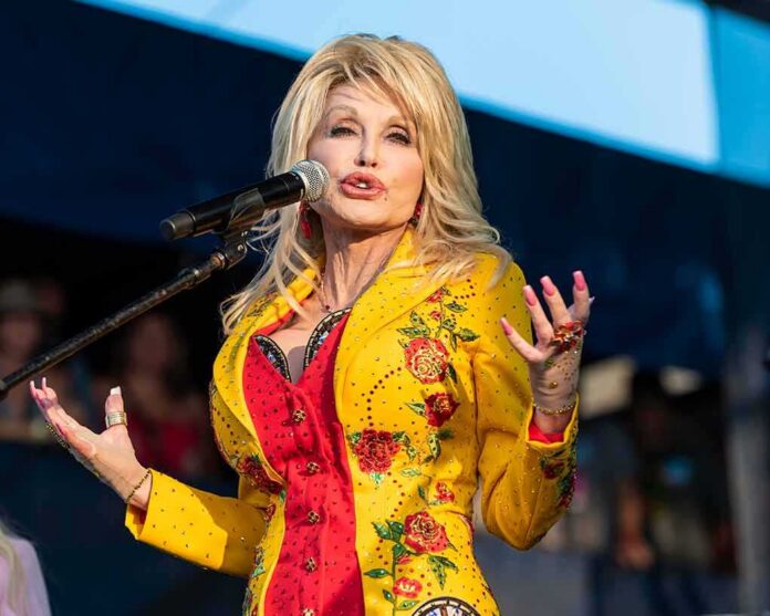 Dolly Parton performing on stage in a yellow floral jacket