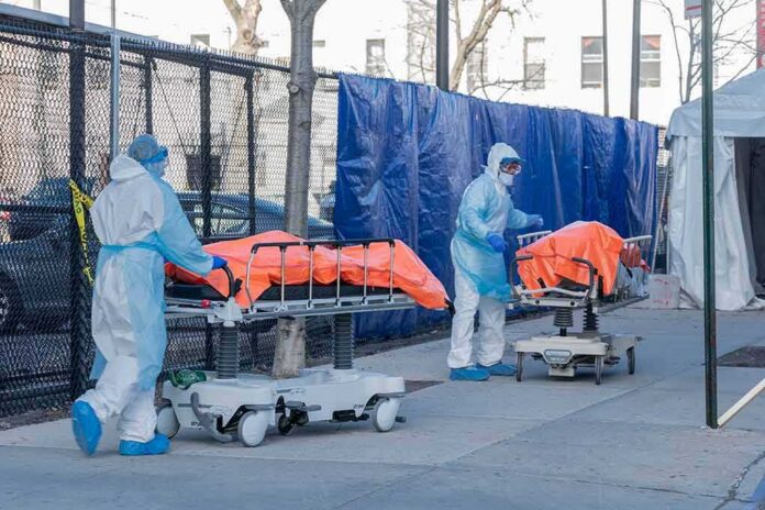 Healthcare workers in PPE move covered stretchers outside a facility